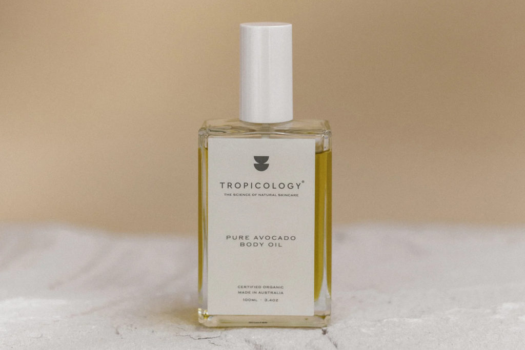 Bottle of body oil on white surface with beige background