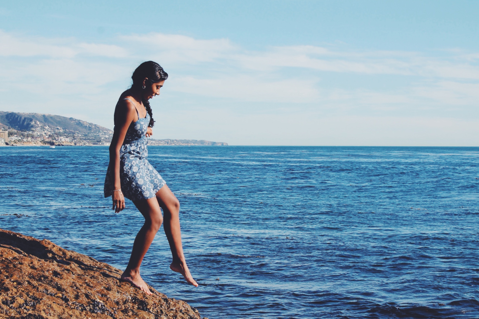 Woman in blie dress dipping foot in ocean from beach mound