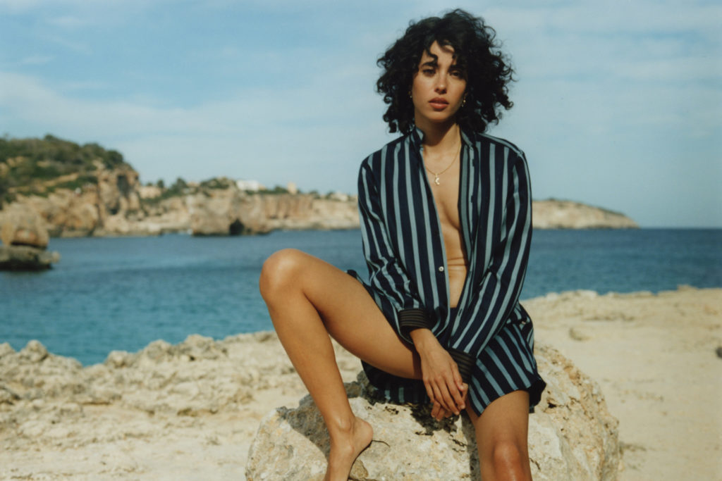 Woman in stripe pj set sat on rocks by ocean