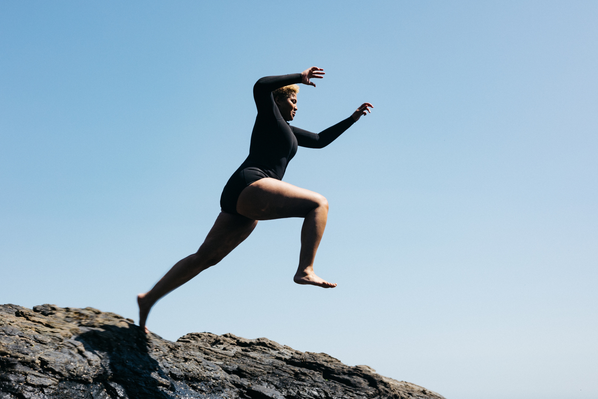 Woman jumping from rocks in wetsuit