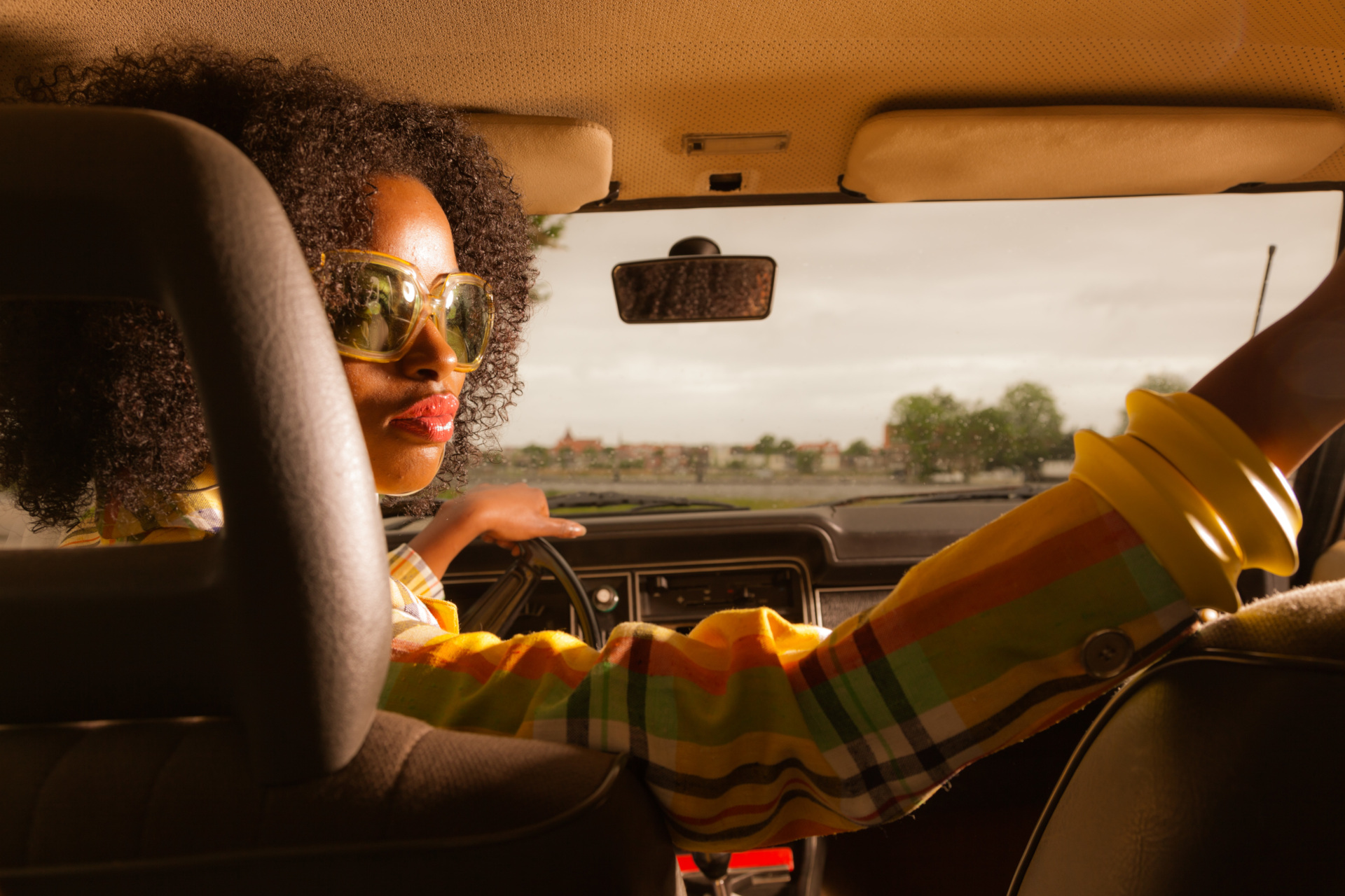 Woman in 70s fashion looking over shoulder as she reverses car