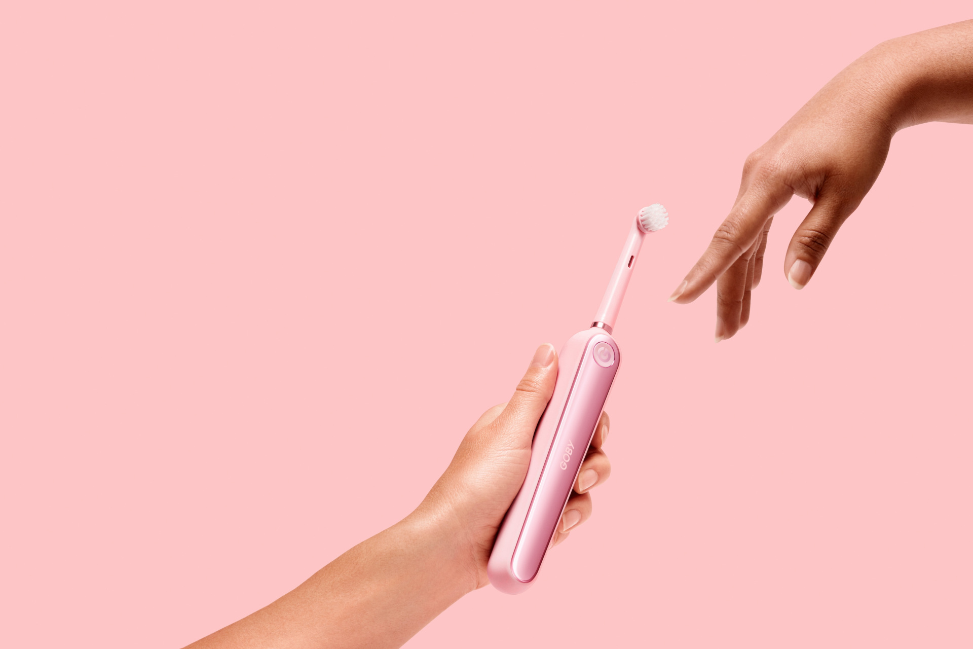 Electric toothbrush being passed between hands on pink backgrounf