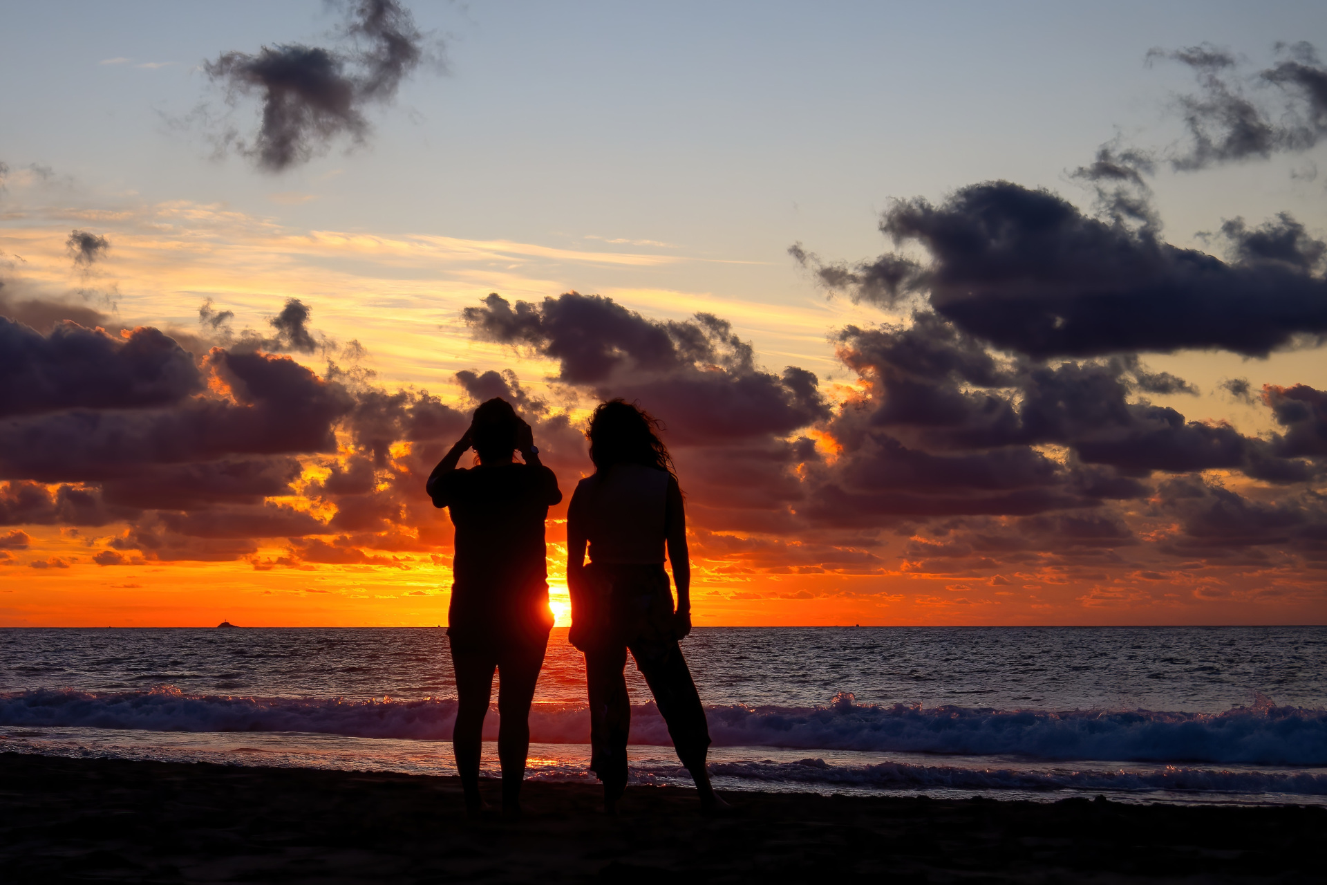 LGBTQ+ couple stood on beach at sunset