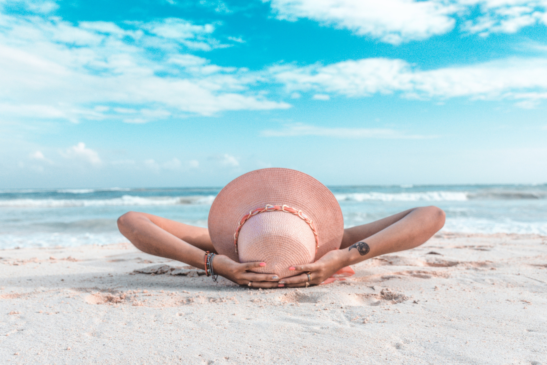 Woman lying down on beach with woven hat on