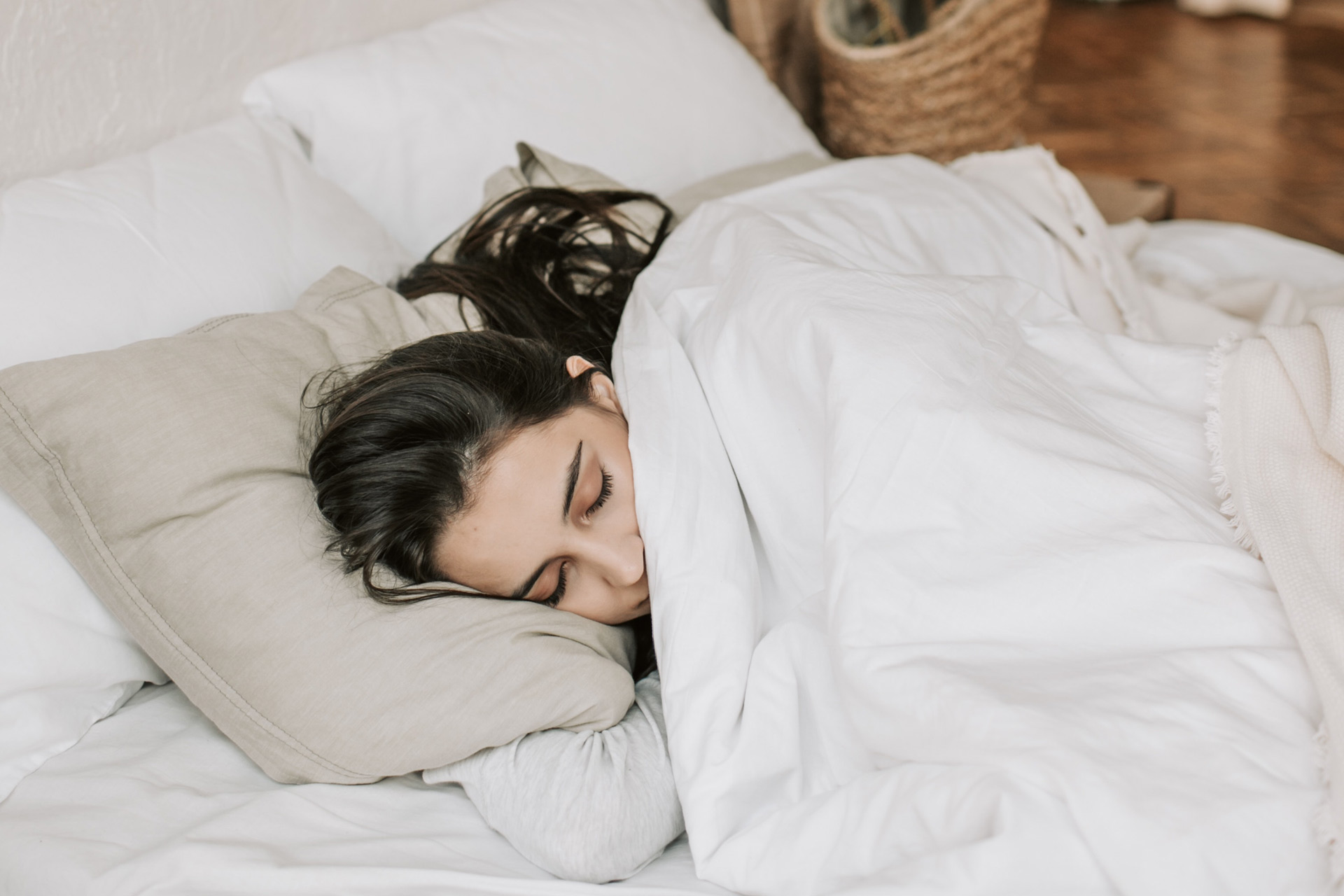 Brunette woman sleeping with beige pillow and white duvet