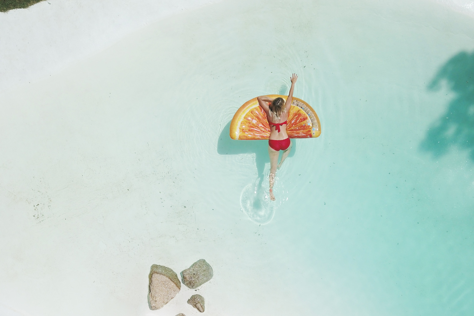 Woman on orange slice float in blue beach water
