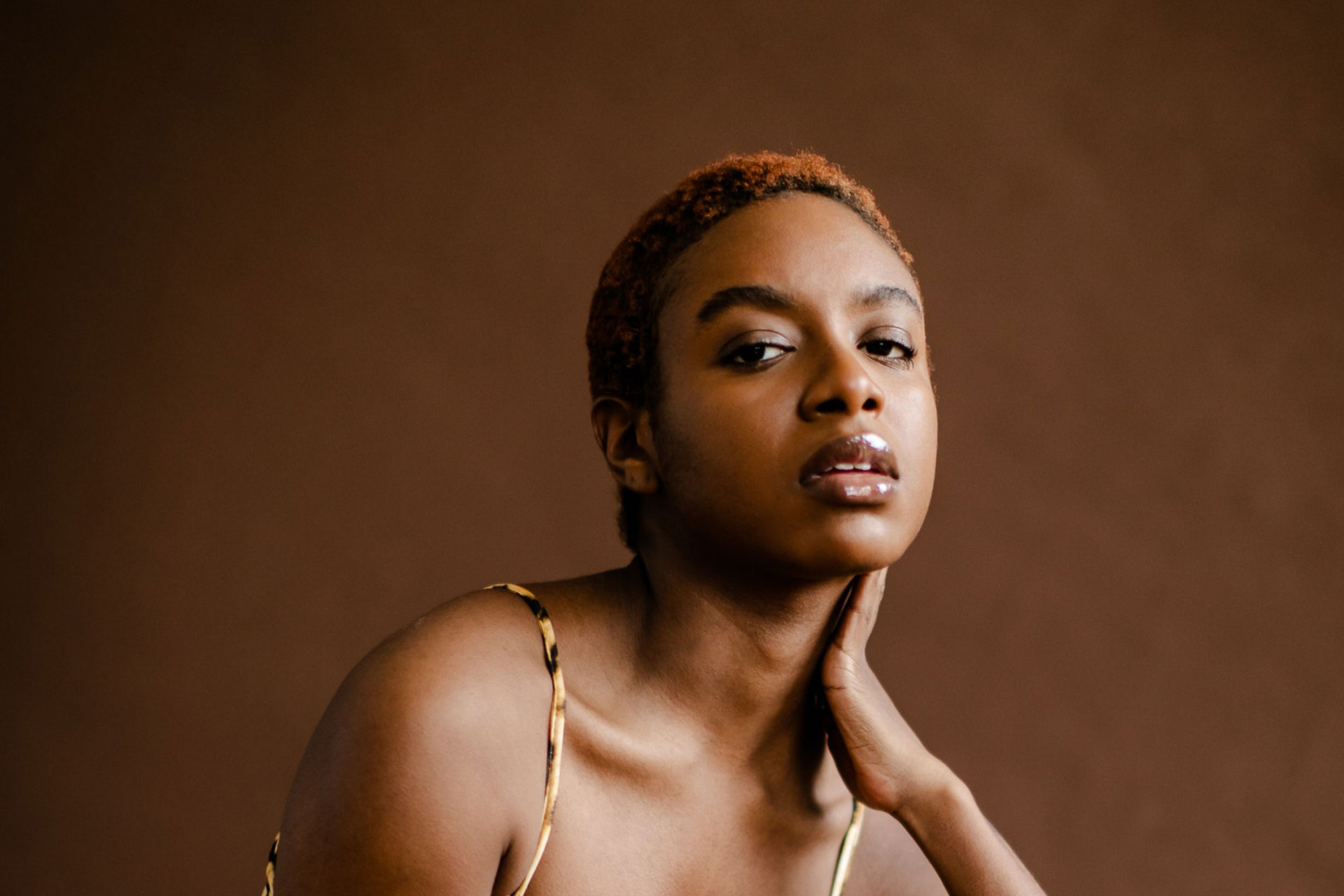 Woman with short hair touching her skin against a brown backdrop