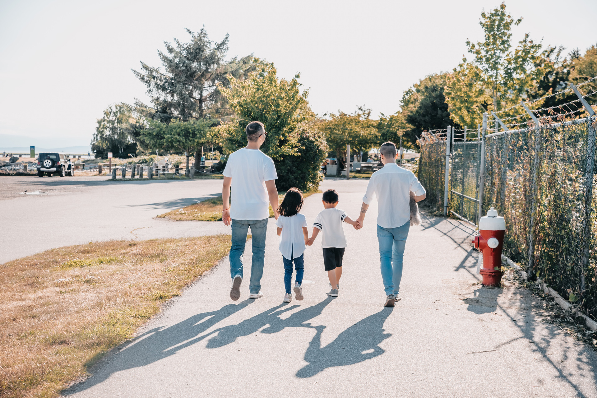 Two dads walking along with their children, holding hands