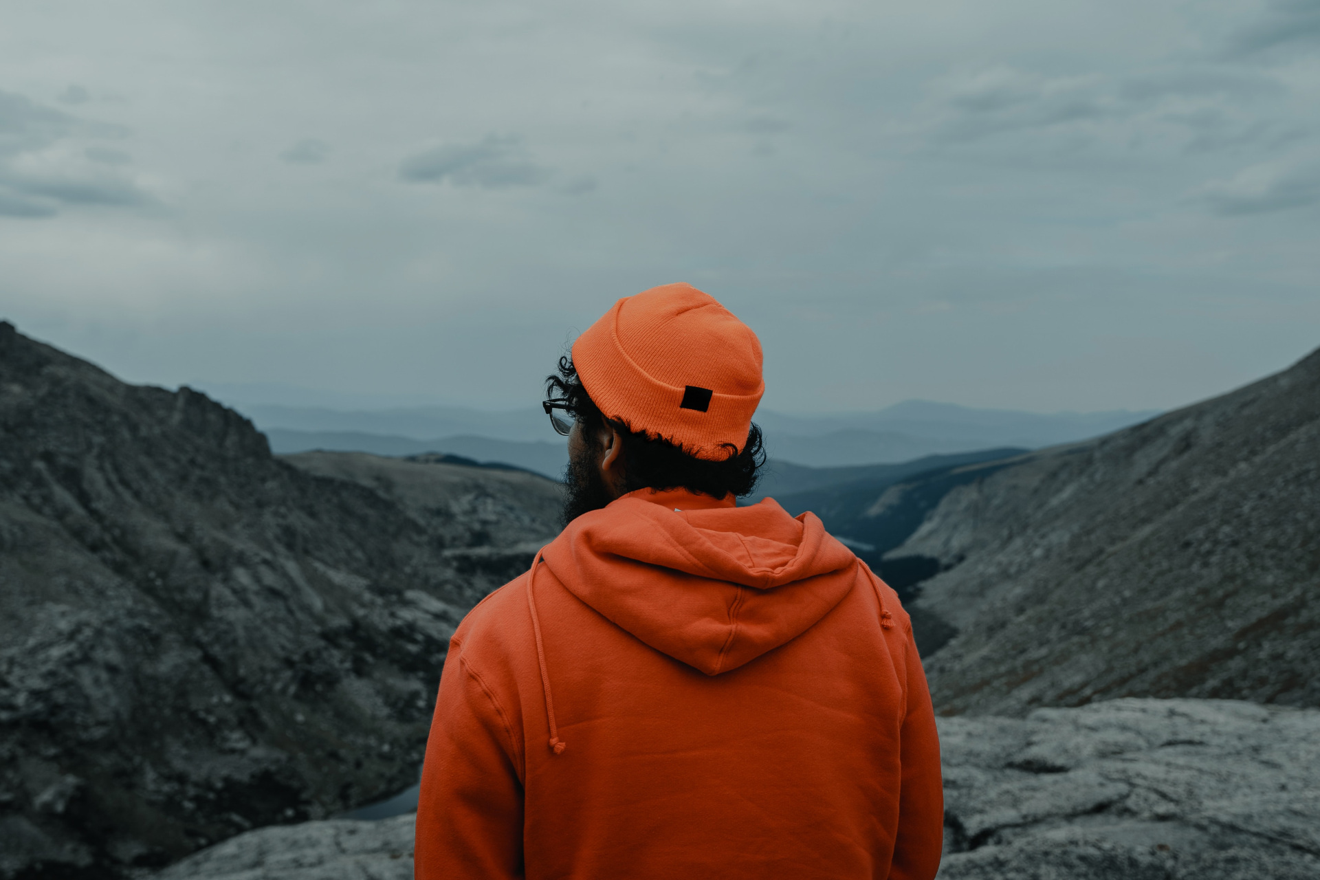 Man in orange hoodie and beanie looking out at mountains