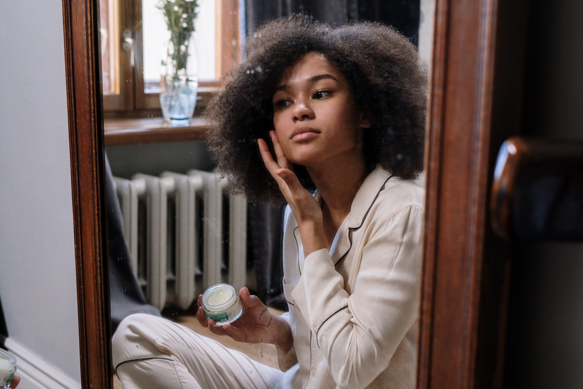 Black woman applying face cream in mirror