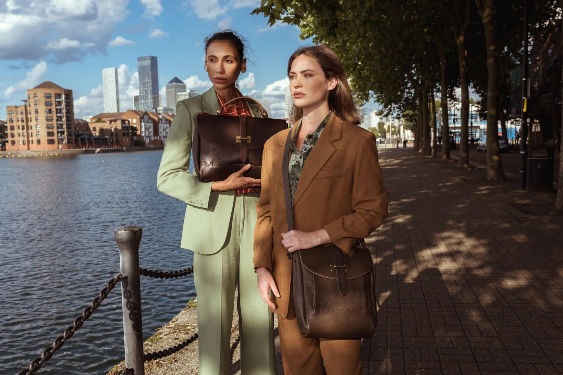Two women stood by Thames in suits carrying leather bags