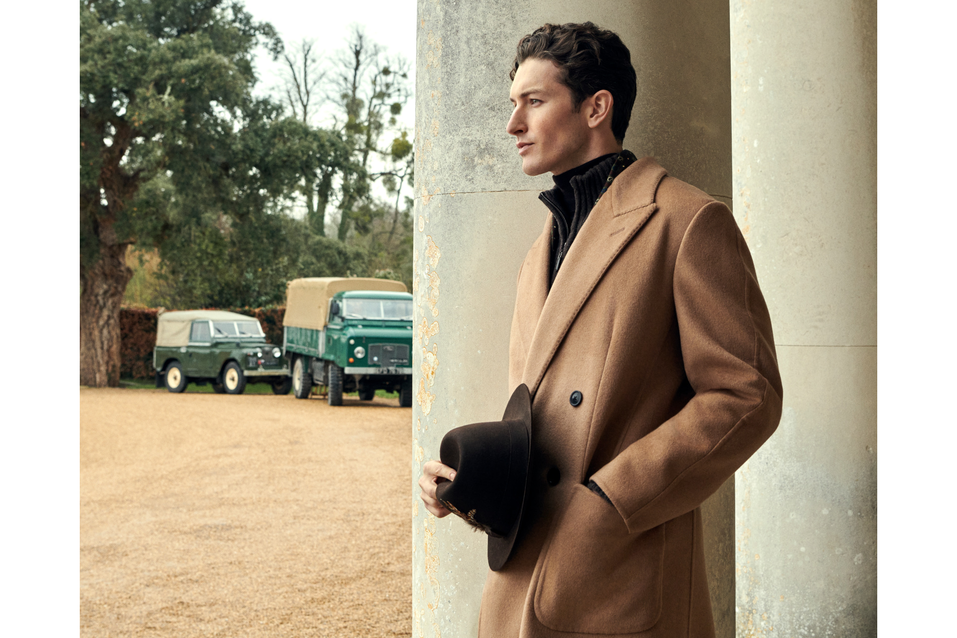 Man in brown coat holding black hat