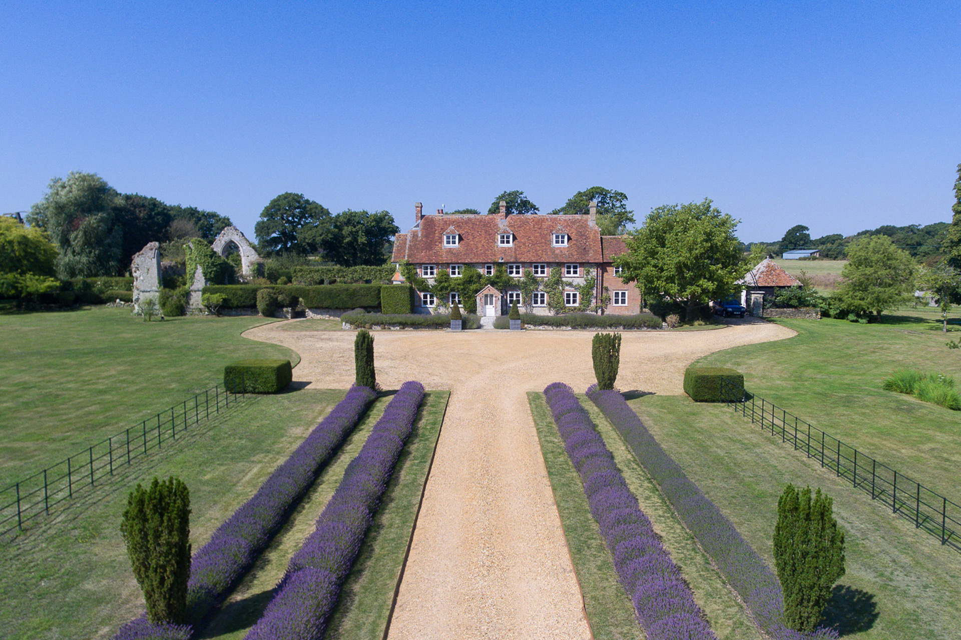 Country home with lavender-bordered driveway and chape ruins beside it.