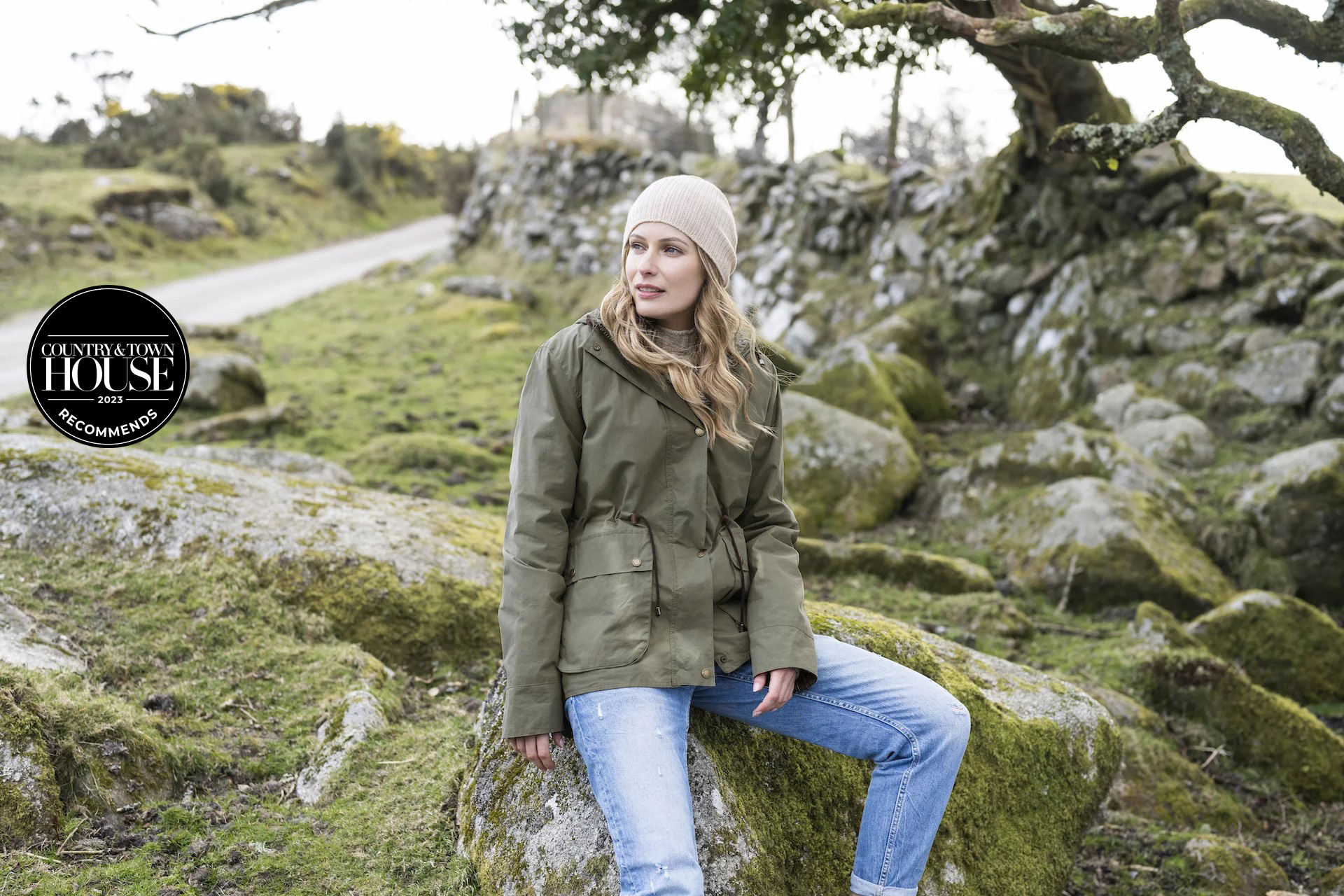 Woman in waxed cotton jacket sitting in a green space | british raincoats