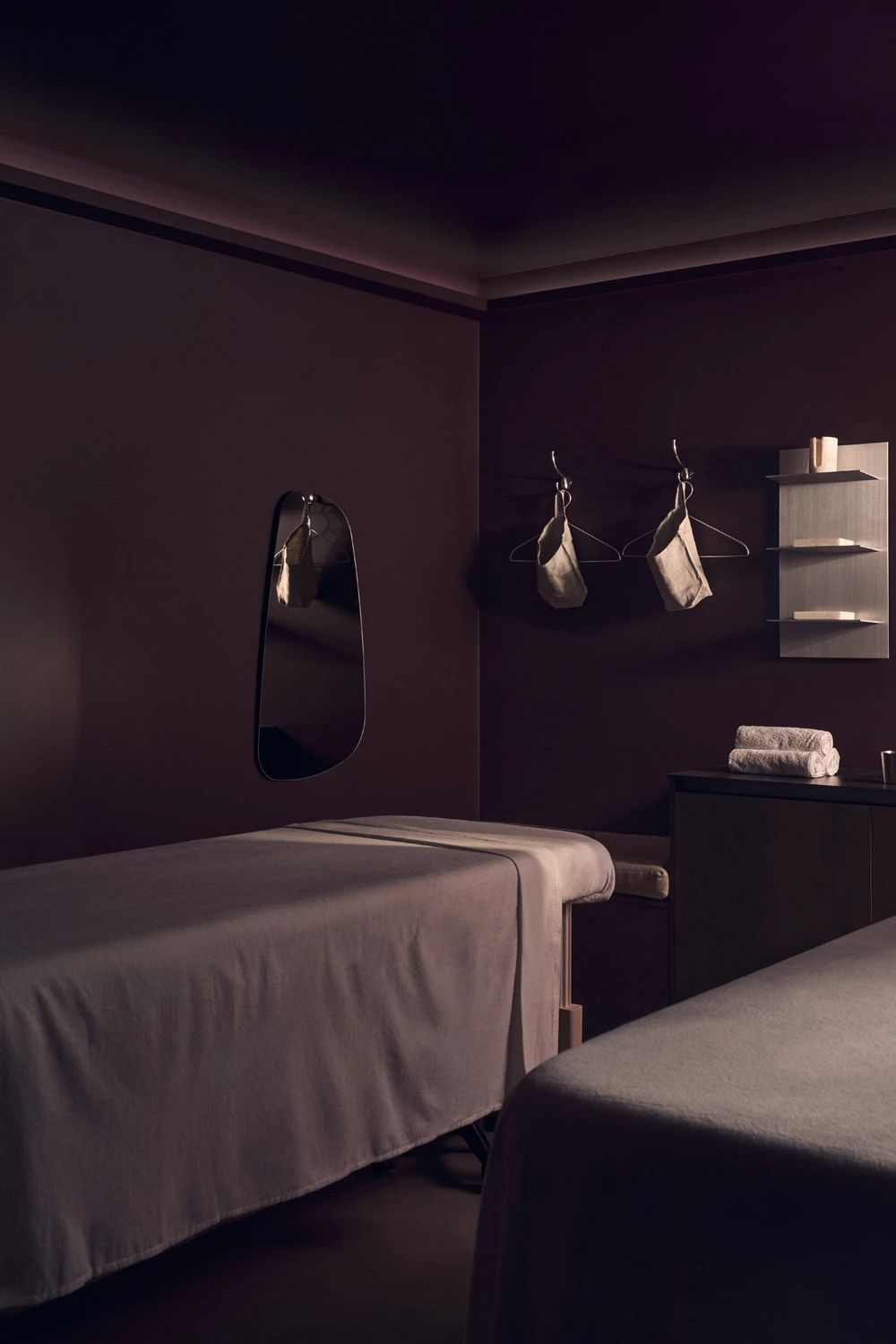 A maroon hued massage treatment room with two beds