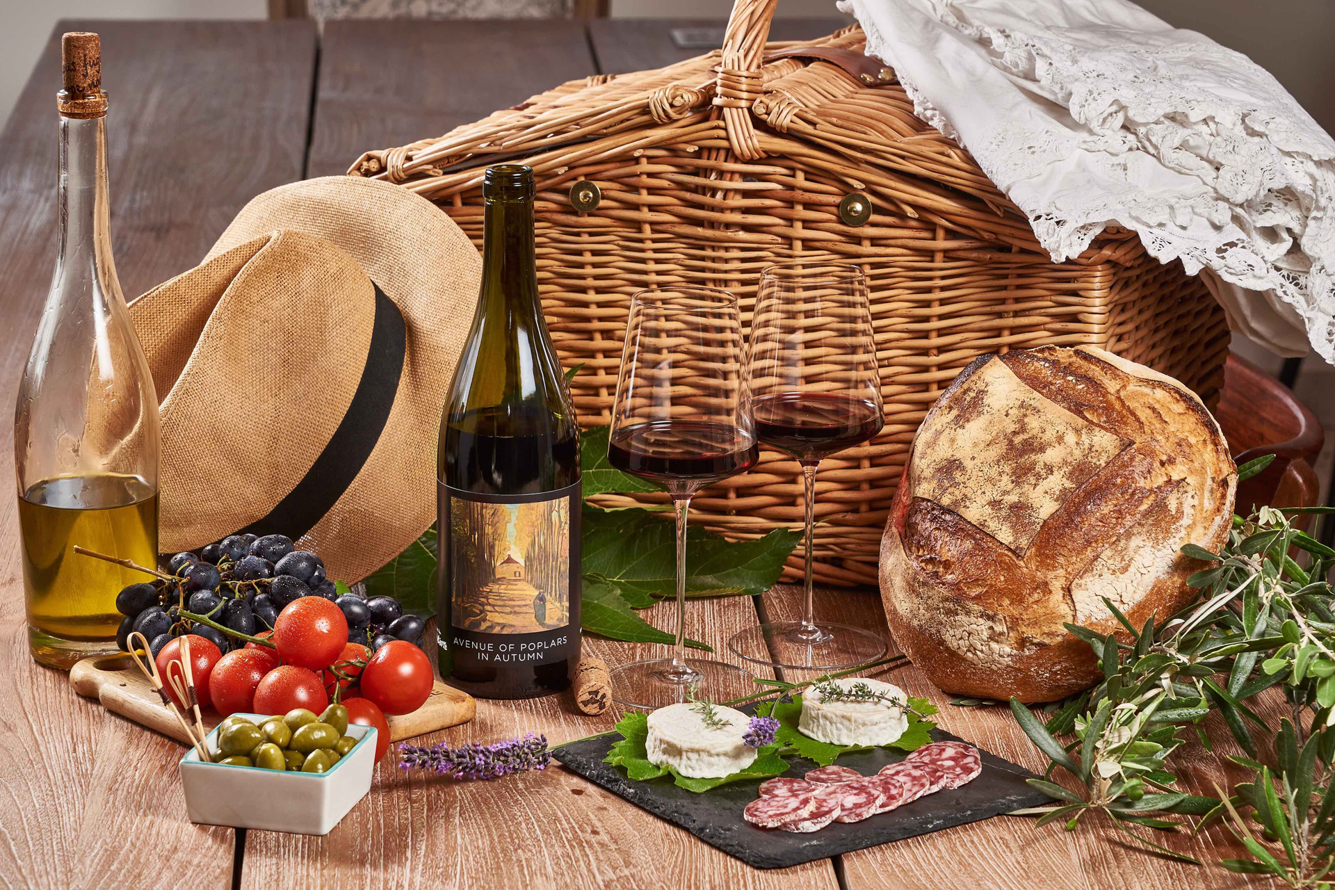 Wine bottle surrounded by picnic items including charcuterie, bread and olive oil.