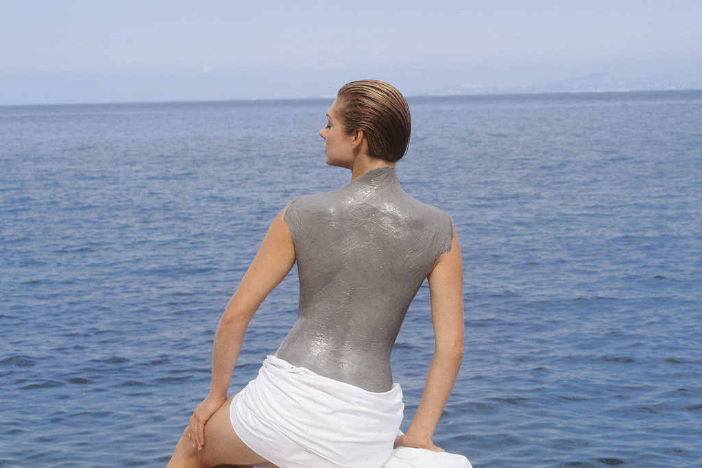 Woman with mud on her back looking out to ocean