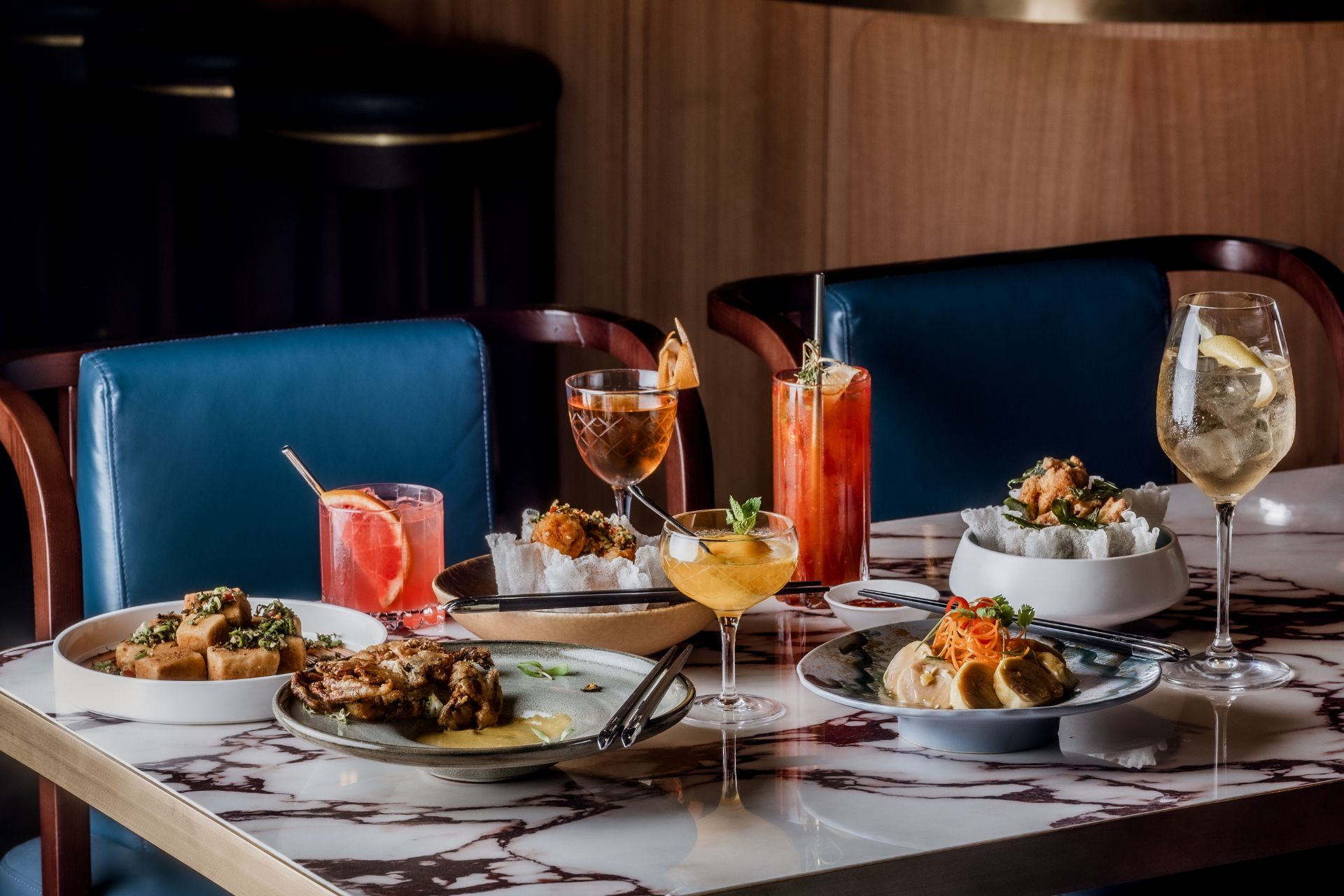 Chinese restaurant with a white marble table, cobalt blue chairs and a variety of dishes and cocktails.