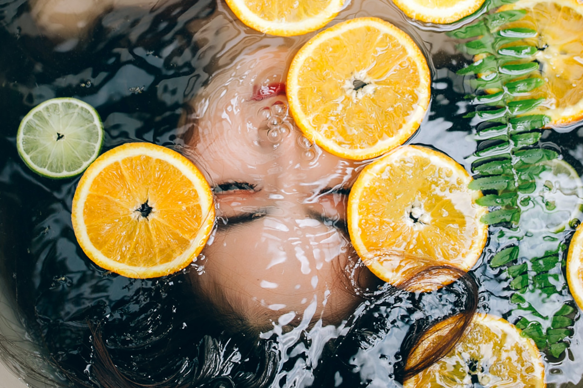 Woman in water with orange slices floating above her face