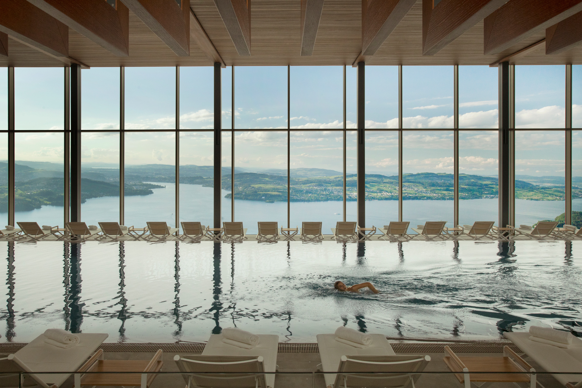 Indoor swimming pool backdropped by floor-to-ceiling windows overlooking lake