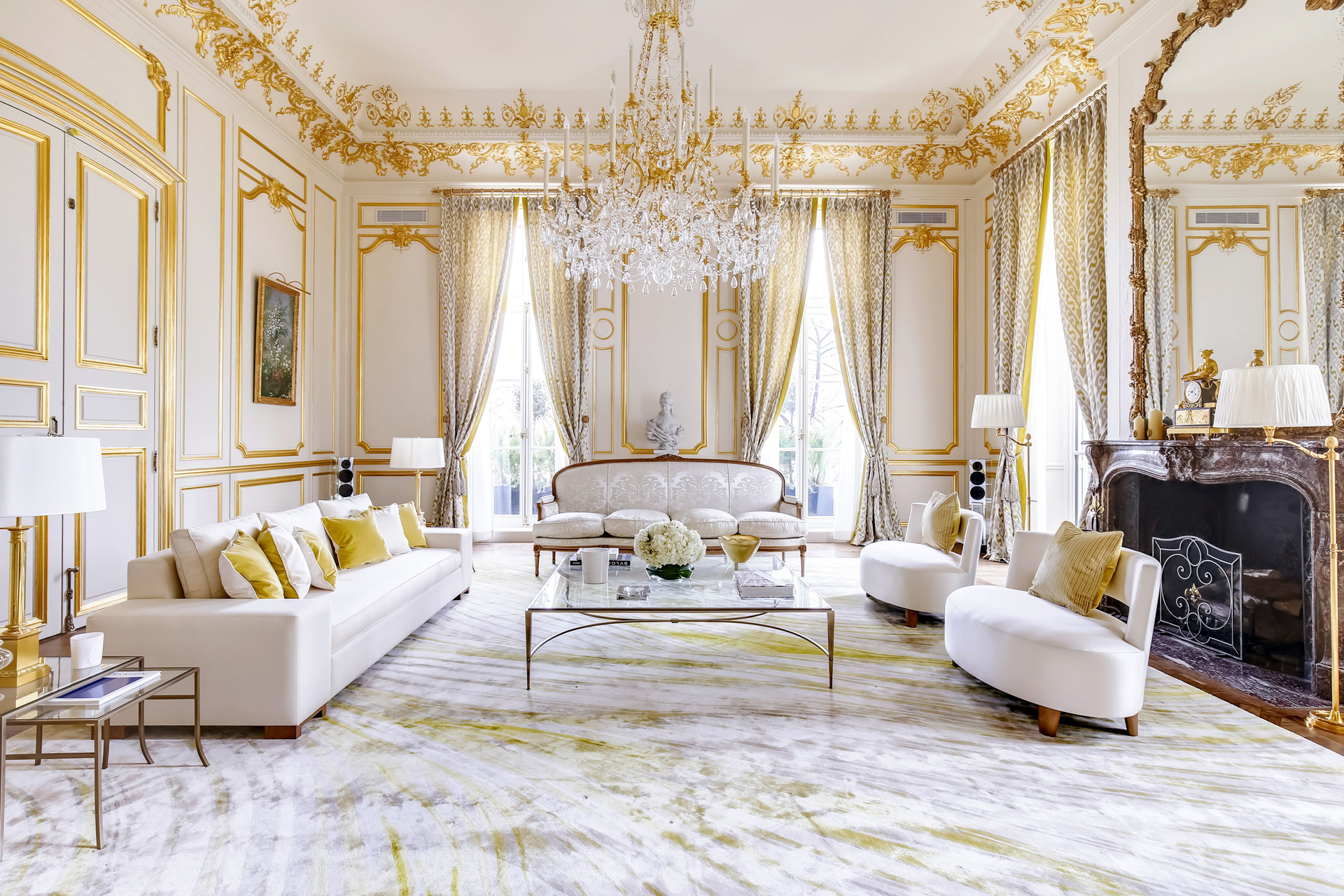 Living room in Paris apartment with white sofas, gilt-edged walls and a stone fireplace.