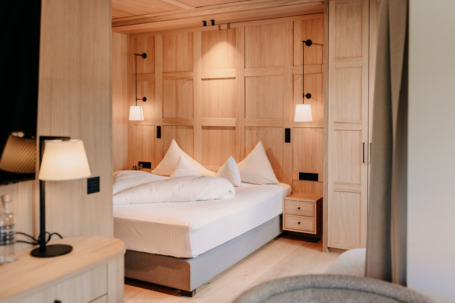 Light wood-panelled bedroom with white linens and soft lighting
