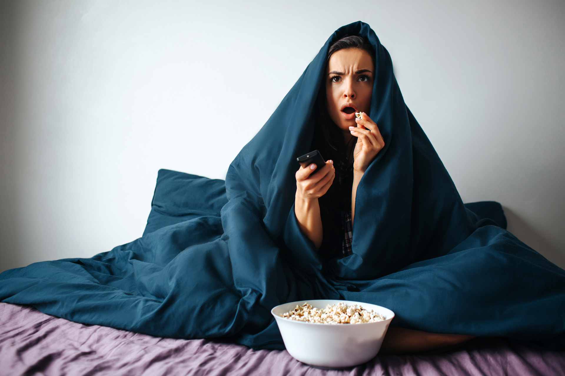Woman watching a scary film behind a blanket with popcorn