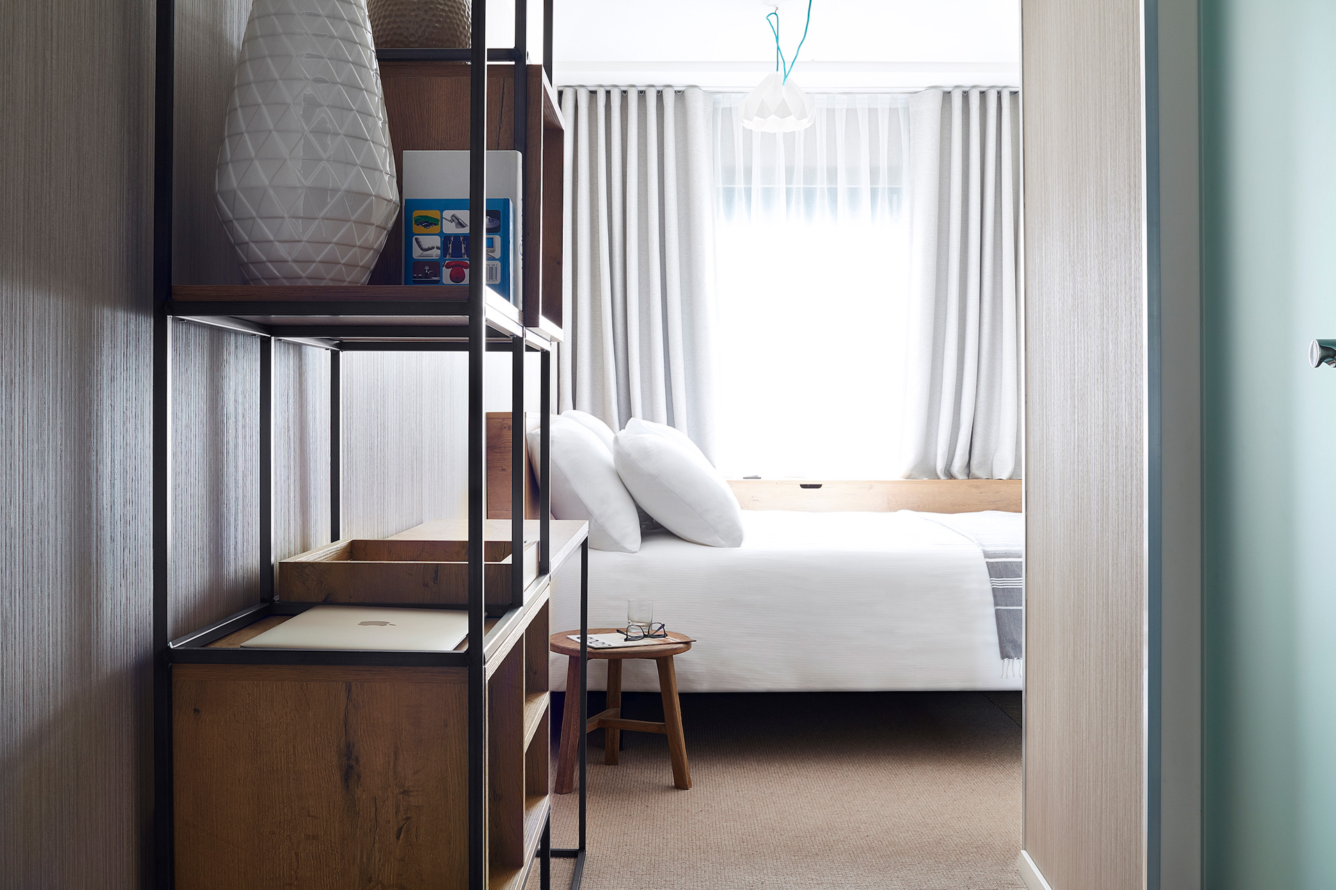 Hotel room with white linens, sheer curtains and dark wooden furniture