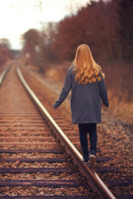 Woman with pumpkin spice ginger hair walking on old train track in autumn
