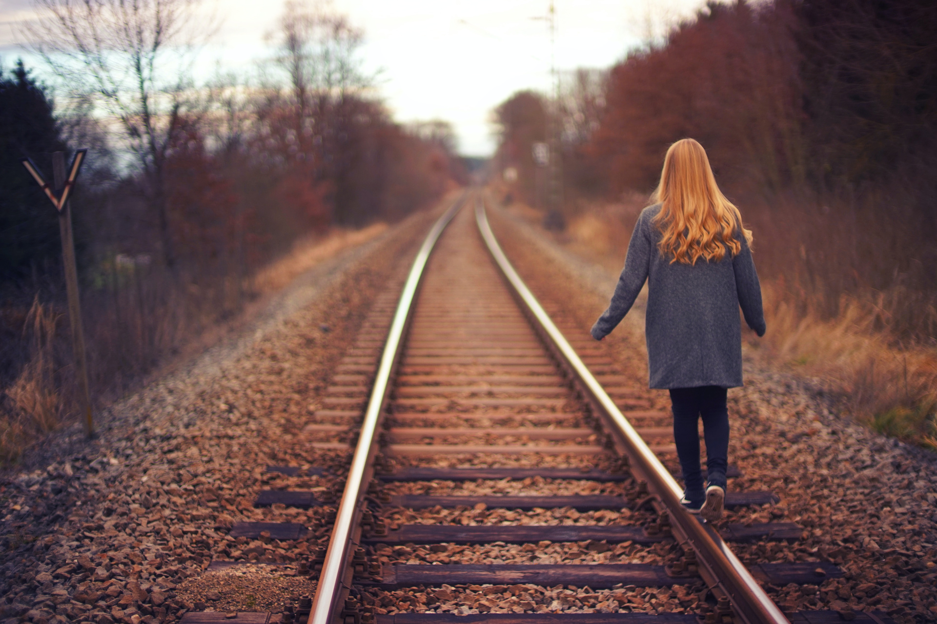 Woman with pumpkin spice ginger hair walking on old train track in autumn