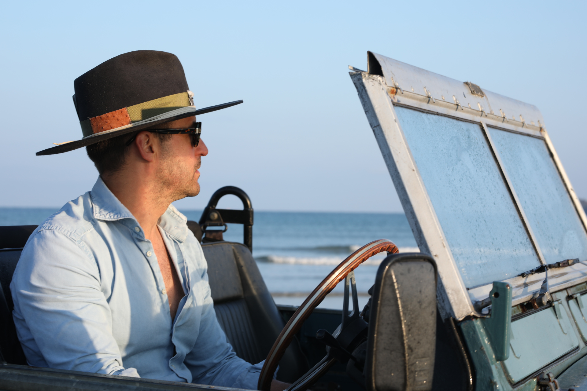 Man sat in car wearing hat, overlooking sea
