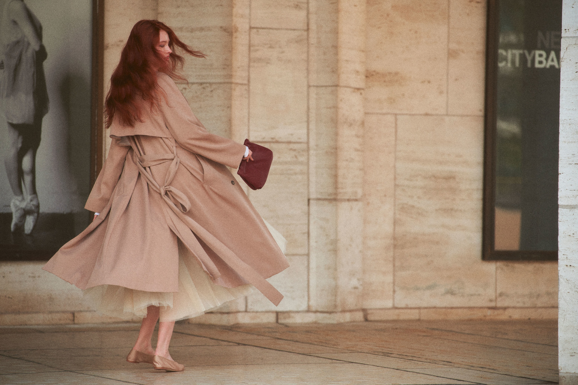 Woman twirling around on street in trench coat and tulle skirt