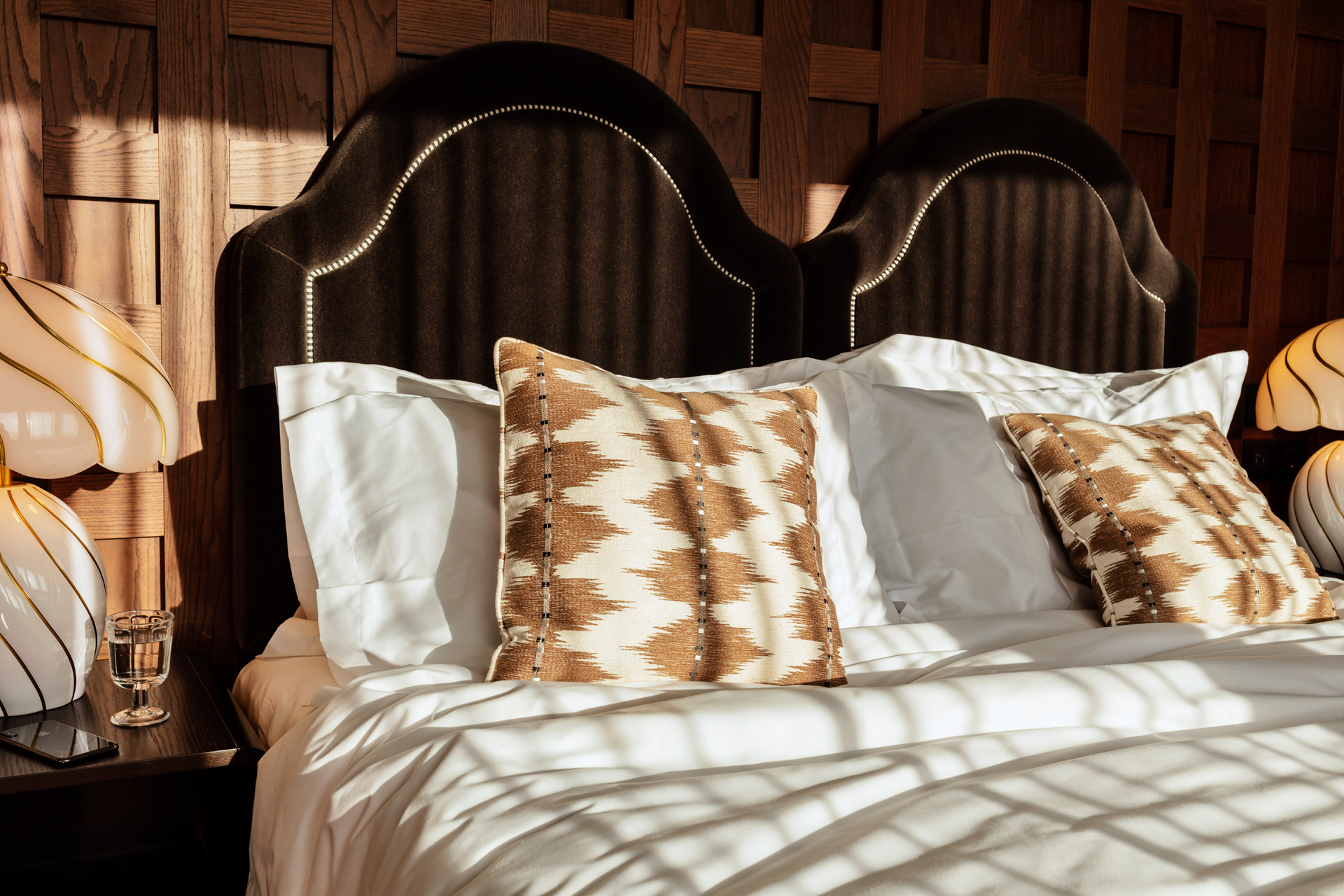 Bedroom at The Hoxton Rome with a dark brown headboard and taupe and white cushions.