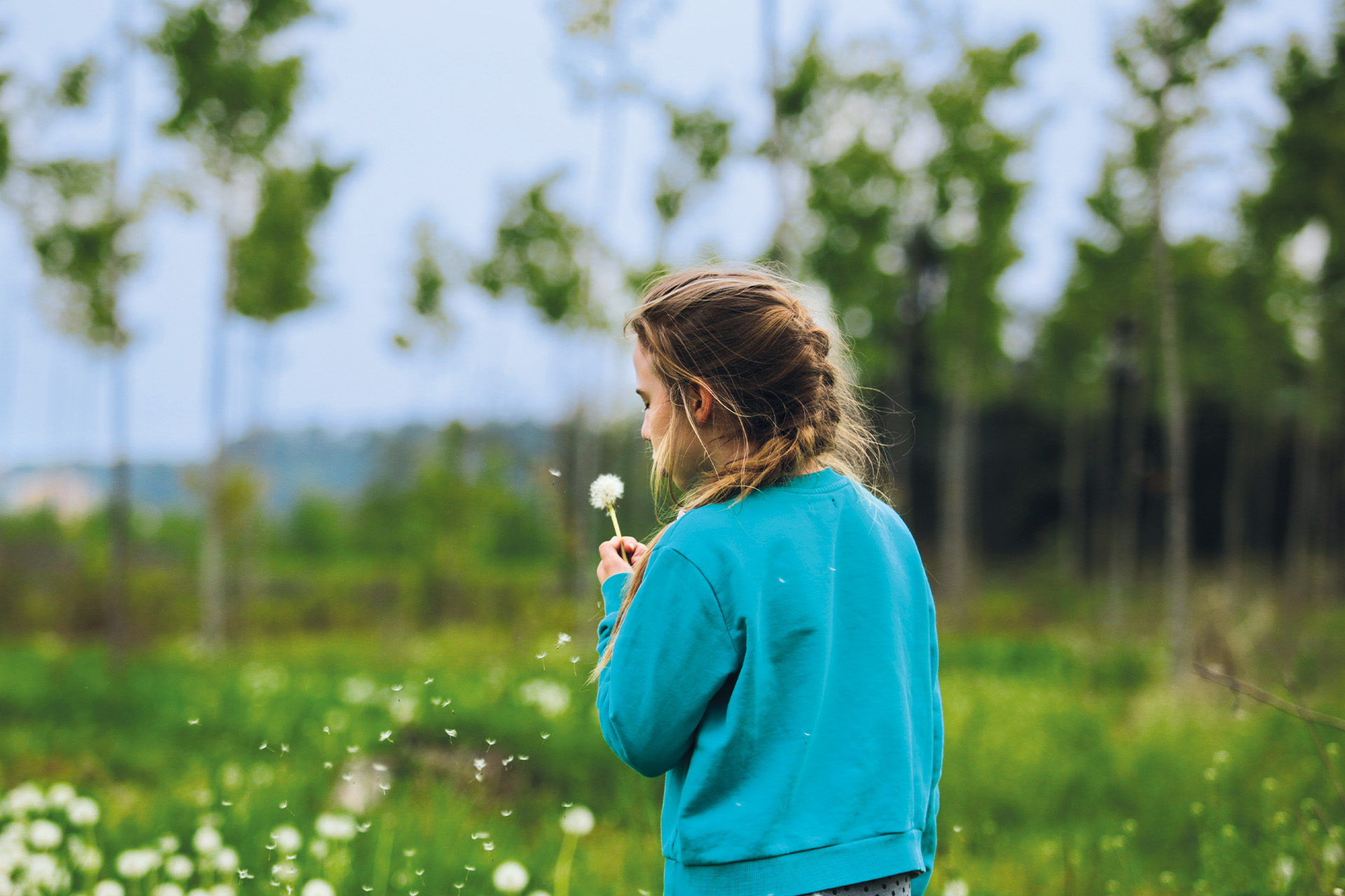 Girl in a field blowing a wishing flower