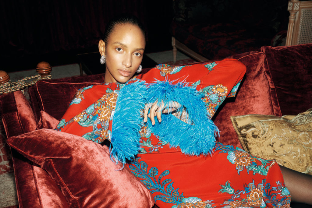 Close up of woman on rust coloured velvet sofa in red and blue dress