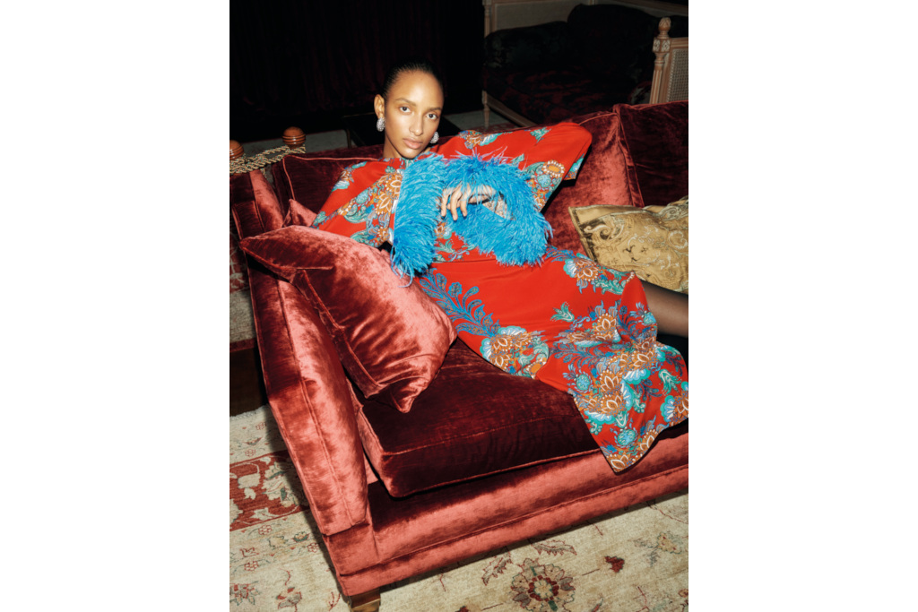 Woman on rust coloured velvet sofa in red and blue dress