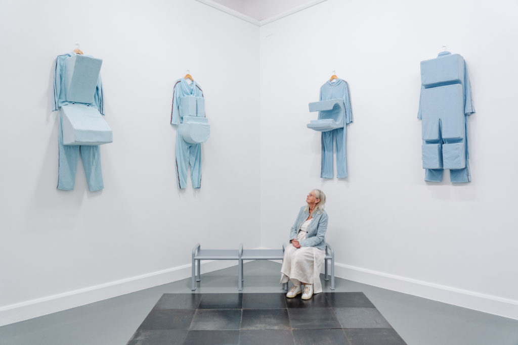 Woman on bench looking up at blue garments hung on white walls
