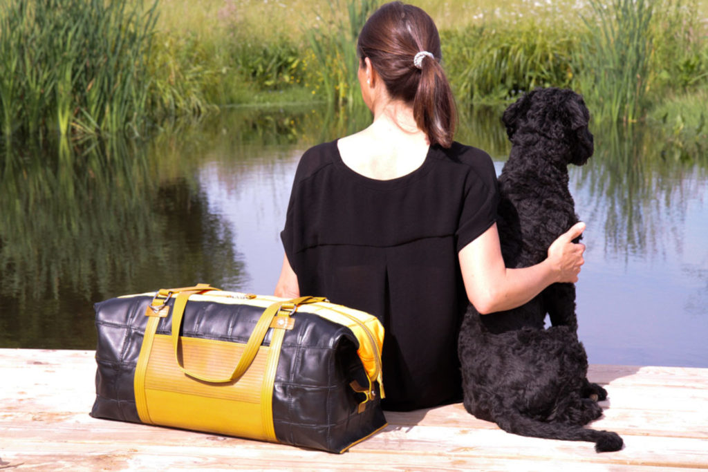 Woman and dog sat by lake with bag