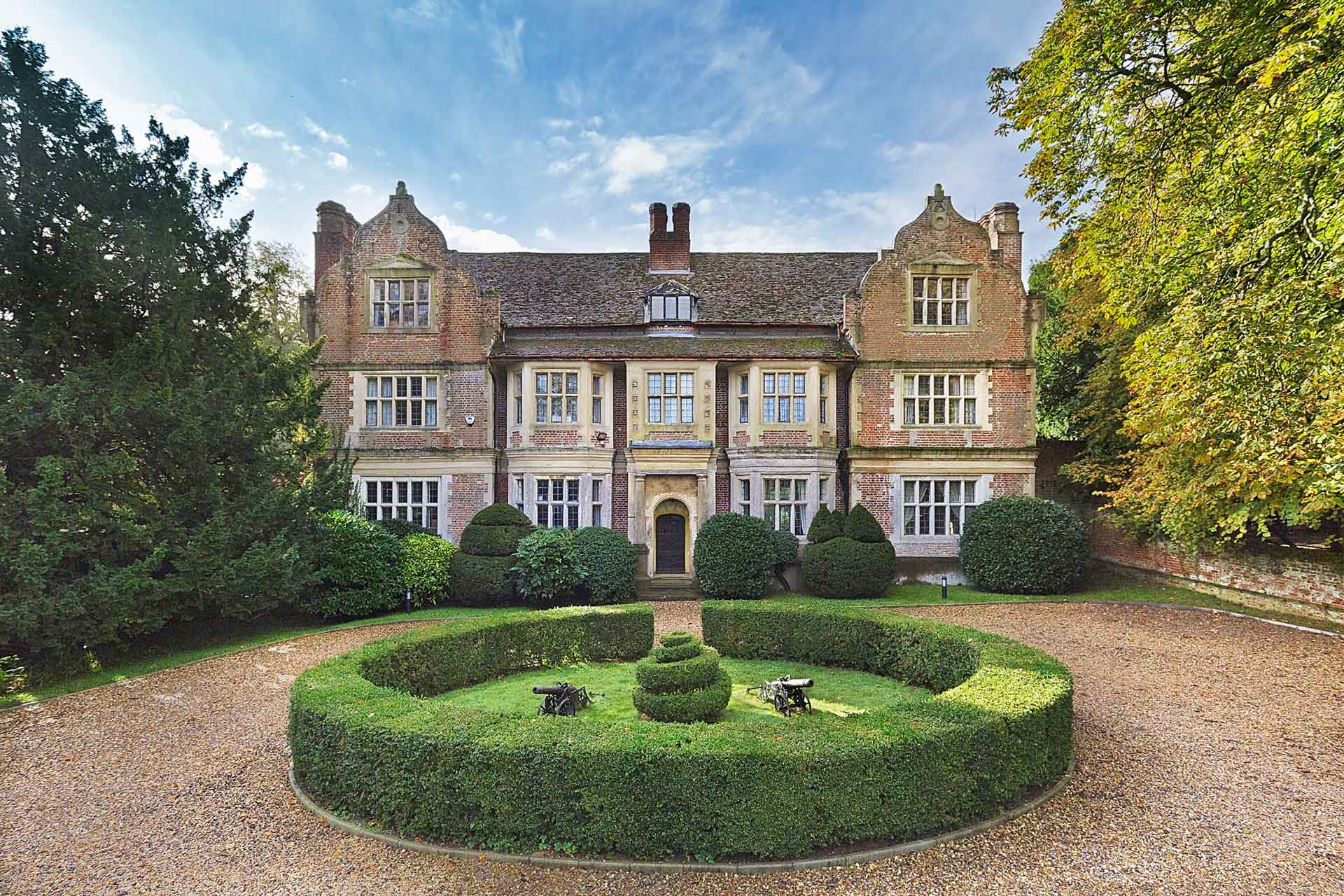 Country manor with Jacobean architecture and a central circular hedge in the driveway.