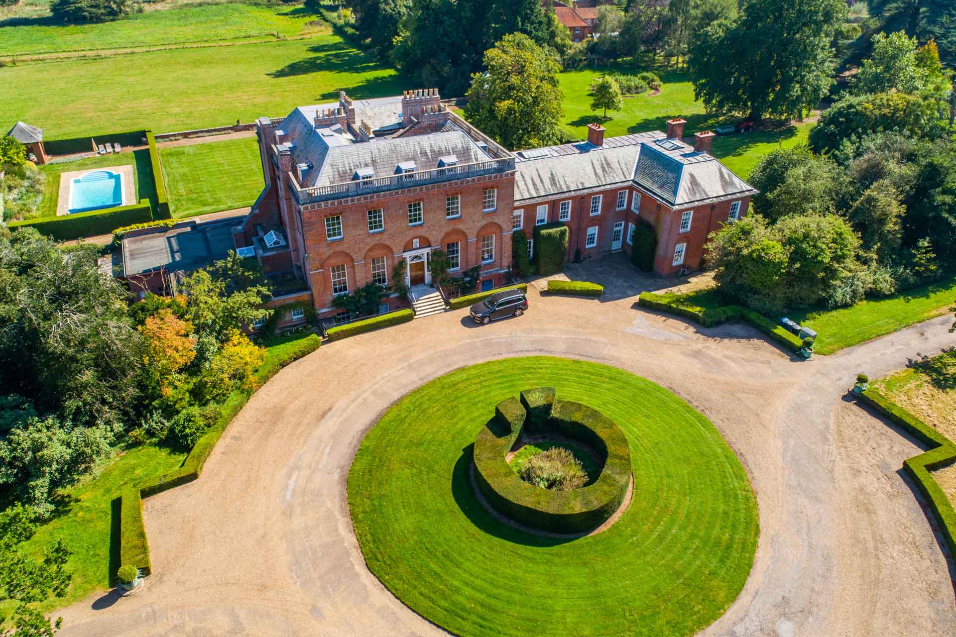 Aerial view of country home with circular driveway, swimming pool and expansive grounds.