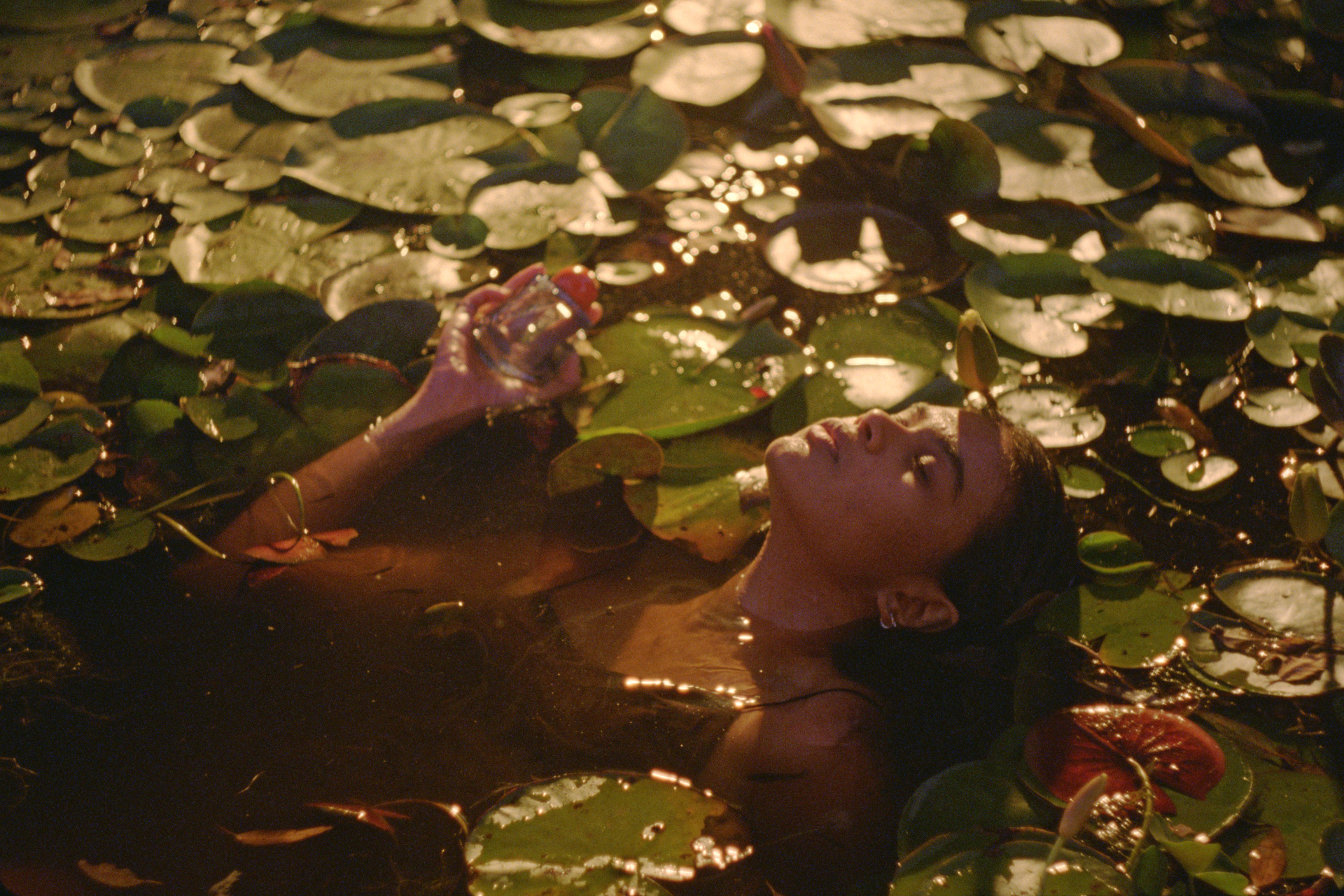 Woman in water and lily pads holding perfume bottle