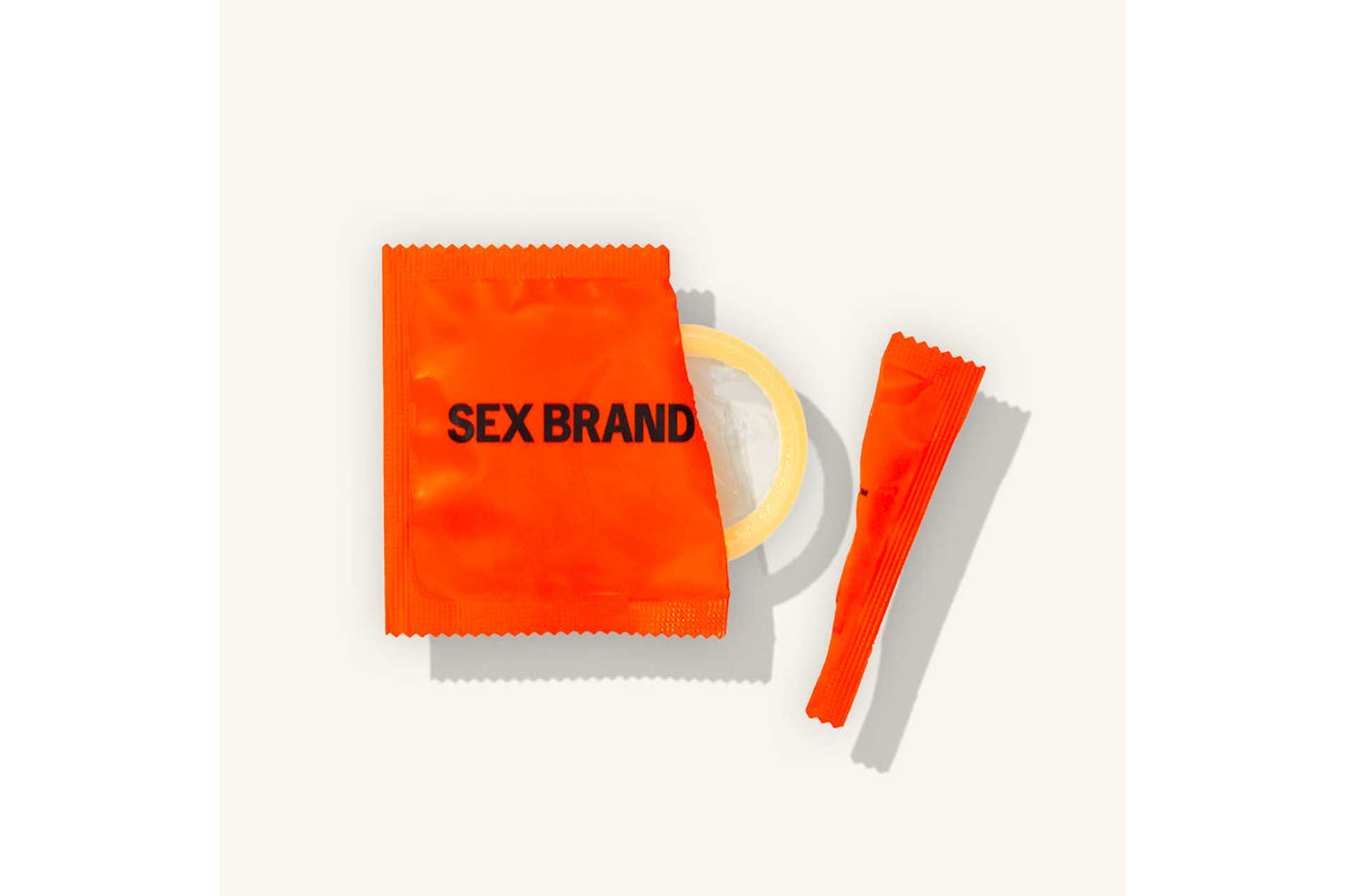 Orange condom wrapper - opened, the condom showing through - with clear caps reading 'SEX BRAND'