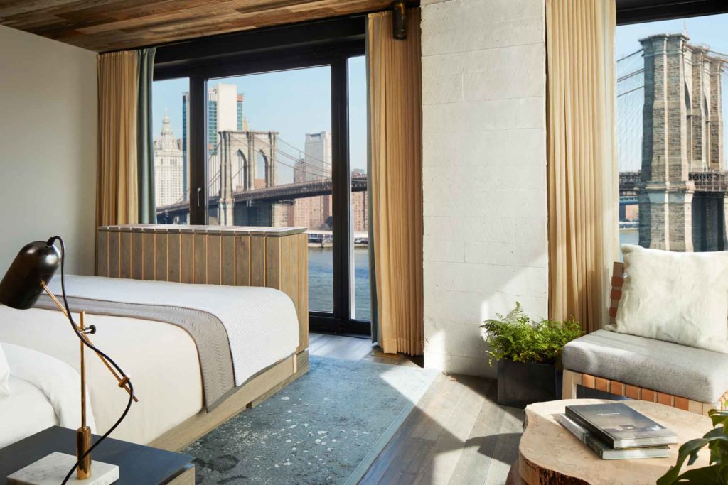 Hotel room with white linen, an armchair and a view of the Brooklyn Bridge