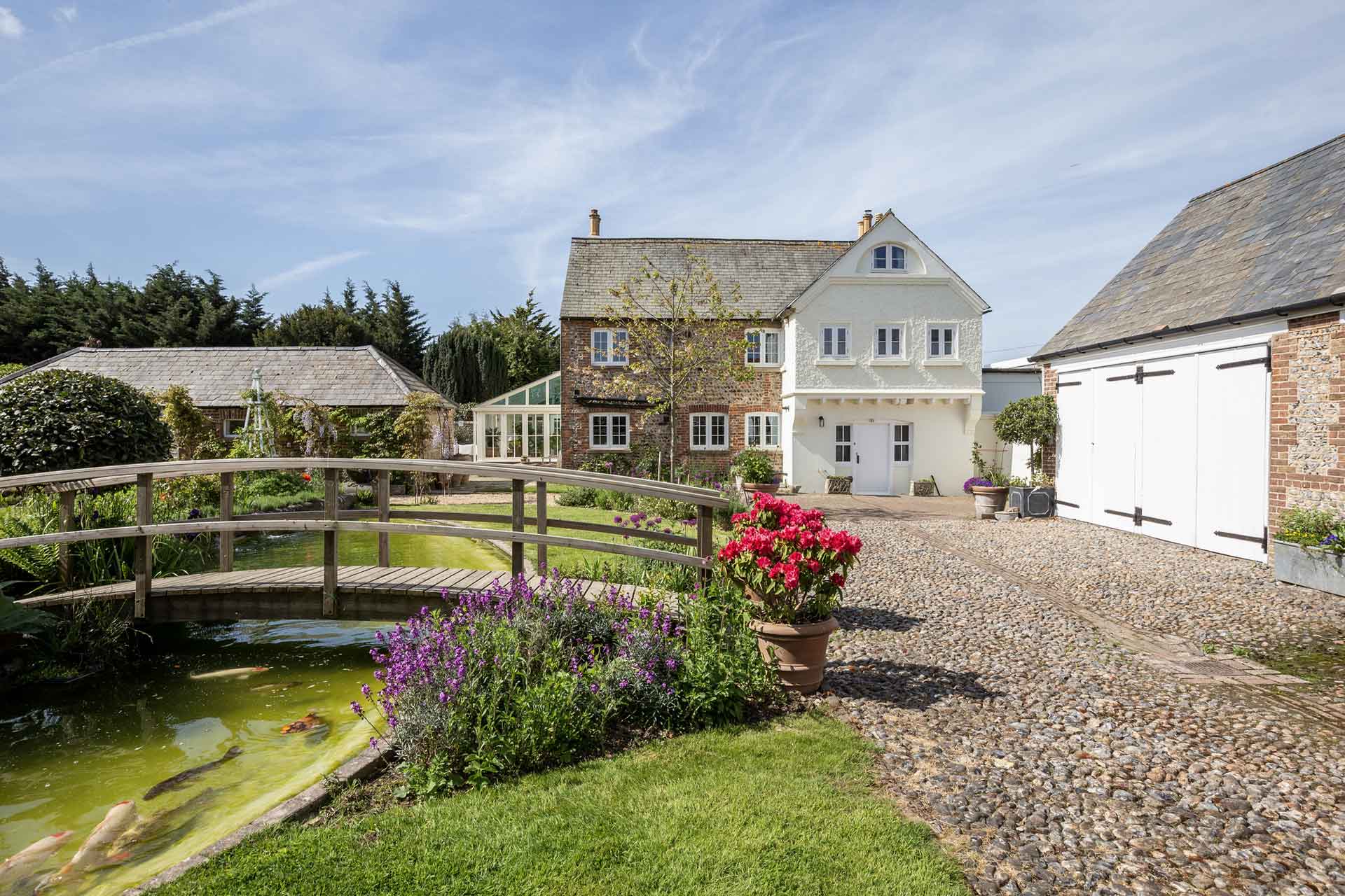 Brick farmhouse with garden, pond and wooden bridge.