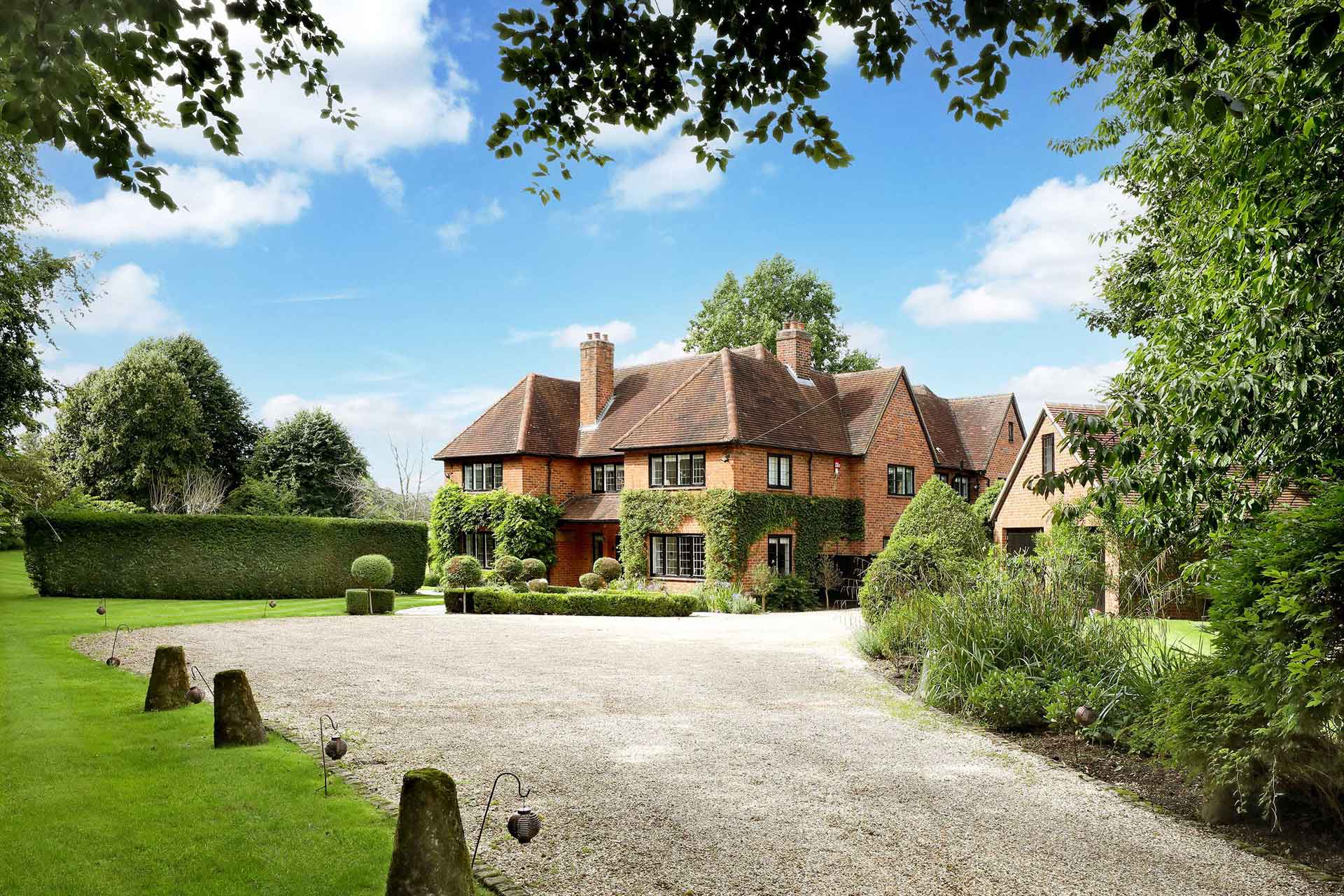 Exterior of country home with gravel driveway and leafy gardens.