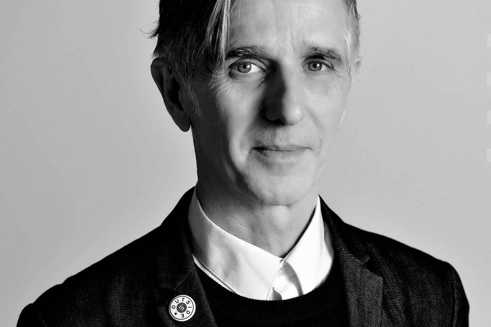 Black and white portrait of Marc Steene with an 'Outside In' badge on his lapel