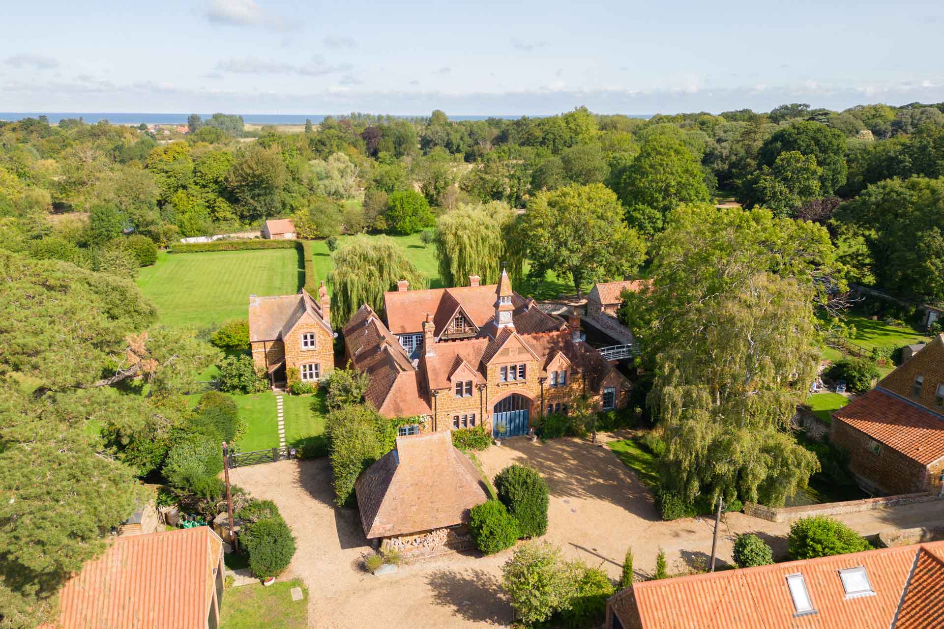 Aerial view of red brick country home with clock tower and woodland surrounding.