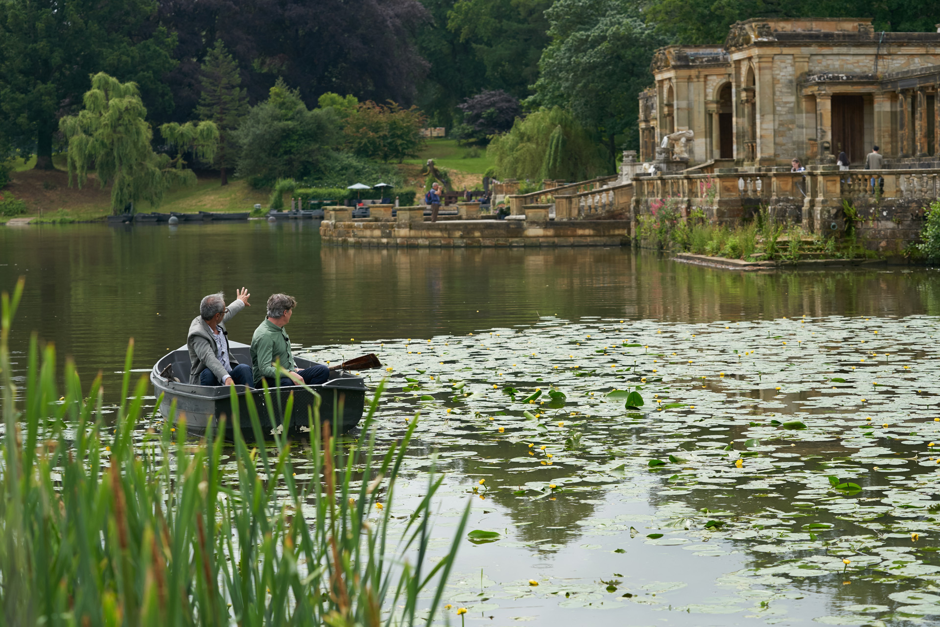 Two men in a boat on a lake with drifting lilypads