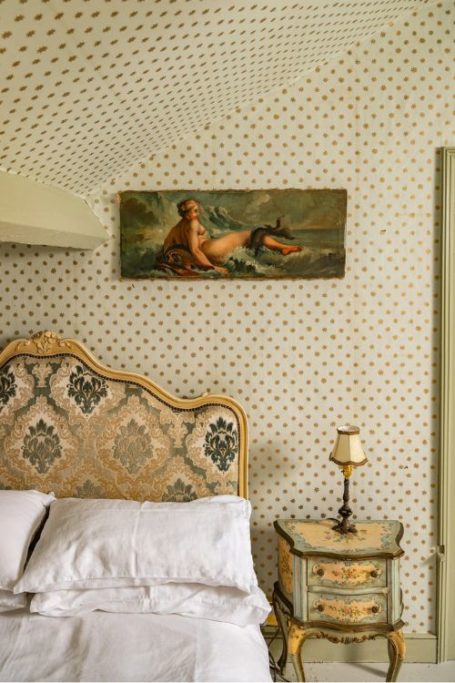 Nude painting on wall with spotted wallpaper and chintzy bed headboard
