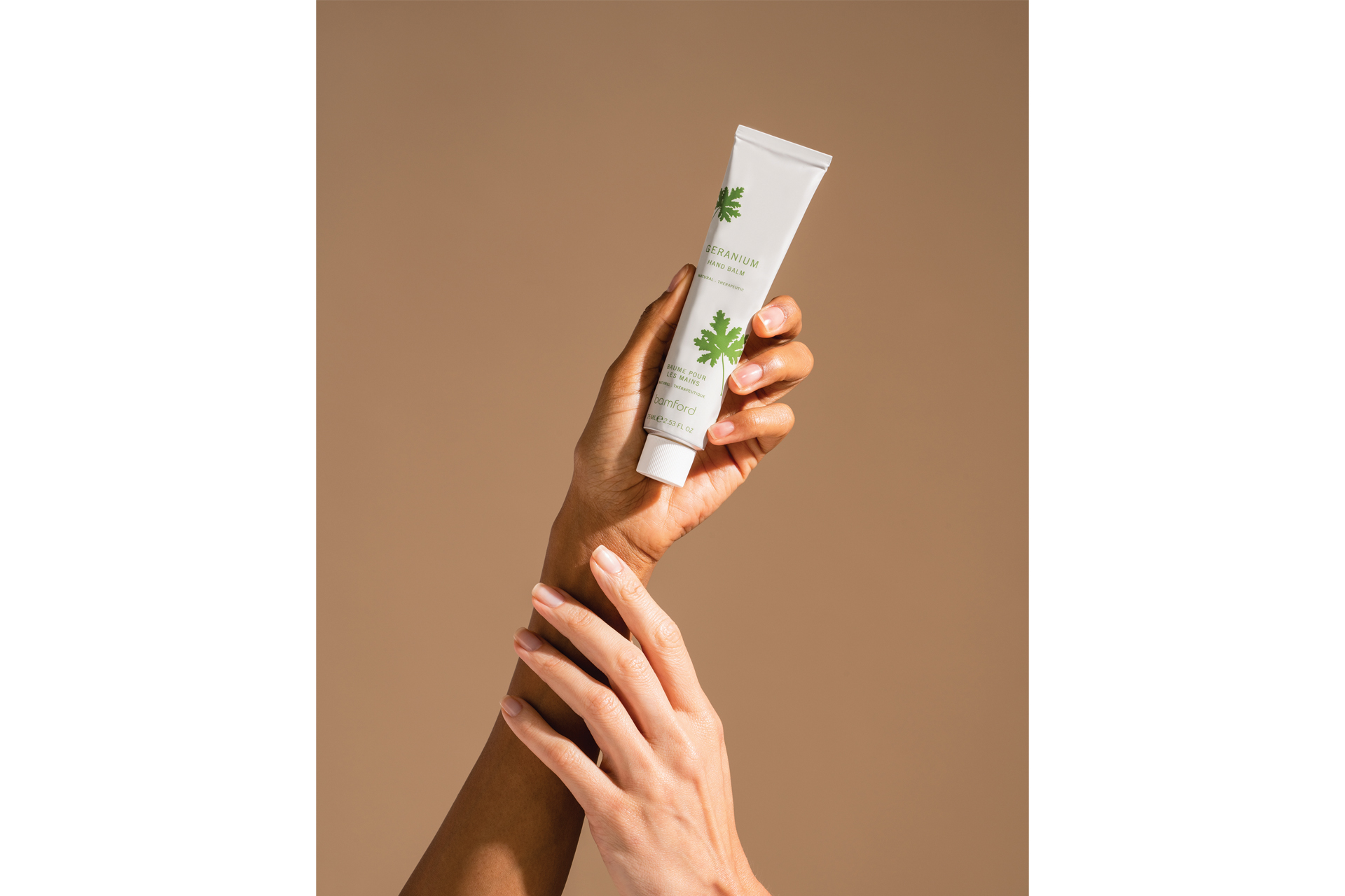 Two hands holding geranium hand cream by Bamford